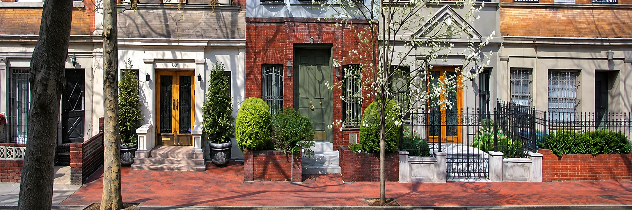 Brick and brownstone townhouses with front stoops along a tree-lined sidewalk