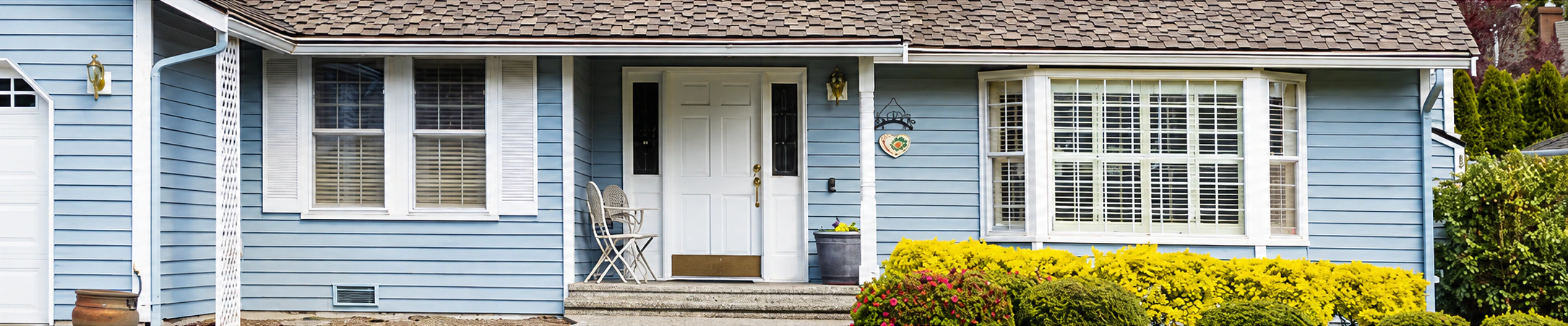 Single-story blue house with a front porch and flowering shrubs